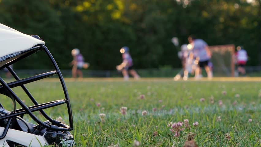 Closeup of lacrosse helmet in the foreground with players and field out of focus in the background. Royalty-Free Stock Footage #1017648724