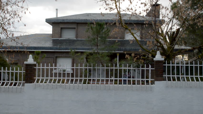 Wide shot of the front façade of a big house with a fence from the street.