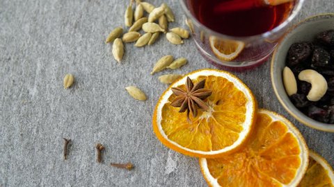 christmas and seasonal drinks concept - hot mulled wine, orange slices, raisins with cashew nuts and aromatic spices on grey background