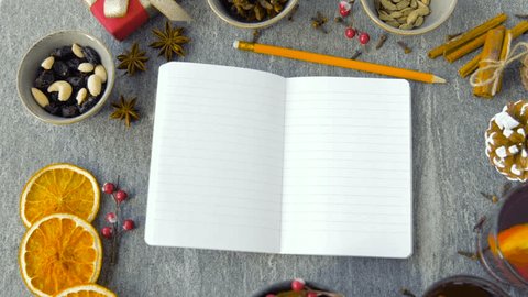 christmas and seasonal drinks concept - notebook with pencil, hot mulled wine and aromatic spices on grey background