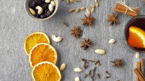 christmas and seasonal drinks concept - hot mulled wine, orange slices, raisins with cashew nuts, gingerbread cookies and aromatic spices on grey background