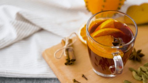 christmas and seasonal drinks concept - glasses of hot mulled wine with orange slices and aromatic spices on kitchen table