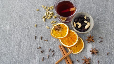 christmas and seasonal drinks concept - hot mulled wine, orange slices, raisins with cashew nuts and aromatic spices on grey background