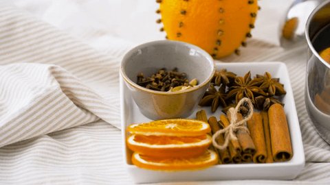 christmas and seasonal drinks concept - aromatic spices, pot of hot mulled wine with orange slices on table cloth or kitchen towel