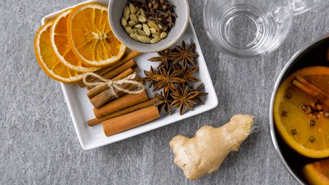 christmas and seasonal drinks concept - pot with hot mulled wine, orange slices, aromatic spices and glass mug on grey background