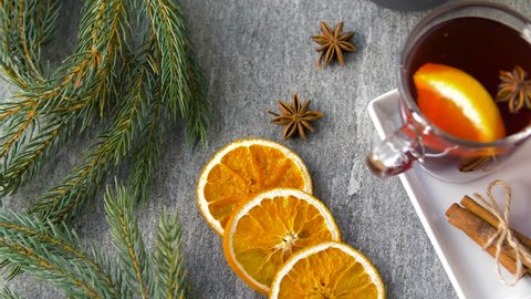 christmas and seasonal drinks concept - glasses of hot mulled wine with orange slices and aromatic spices and fir branch on grey background