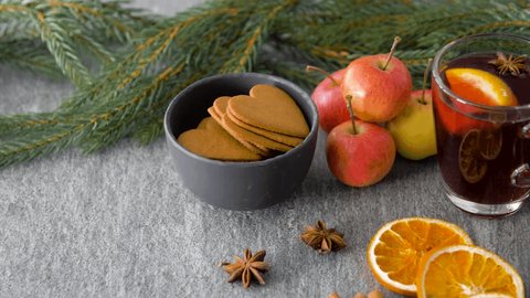 christmas and seasonal treats concept - glass of hot mulled wine with orange slice, gingerbread cookies, apples and fir branch on grey background