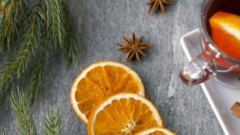 christmas and seasonal drinks concept - glasses of hot mulled wine with orange slices and aromatic spices and fir branch on grey background