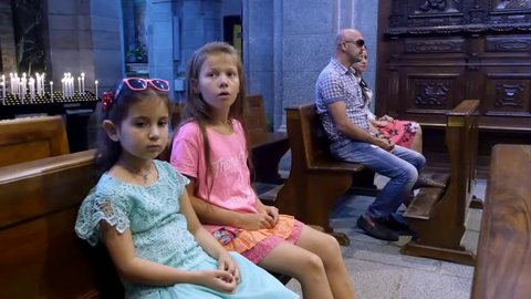 OROPA, BIELLA, ITALY - JULY 7, 2018: people, children and adults are sitting on a benches in a catholic old church, looking at the altar and wall paintings. Shrine of Oropa, Sanctuary, in the