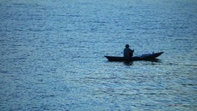 Fisherman in a small wooden fishing boat with light reflecting off the water, low light night fishing high definition stock footage clip. Single fisherman silhouette.