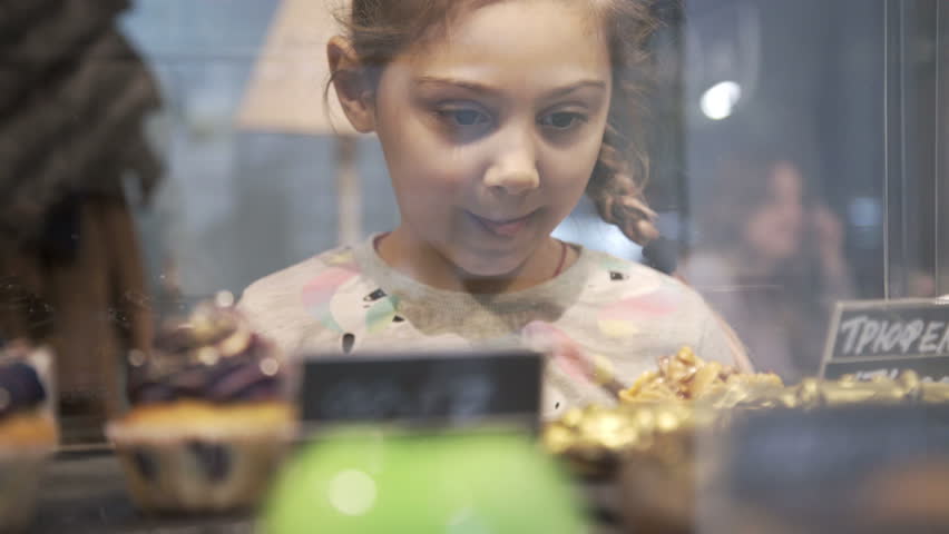 Little girl chosen Cake and desserts. Window of cake shop with variety of cakes on display