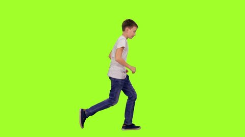 Teenage boy in white t-shirt and jeans running on green chroma key background, Side view, 4k pre-keyed footage
