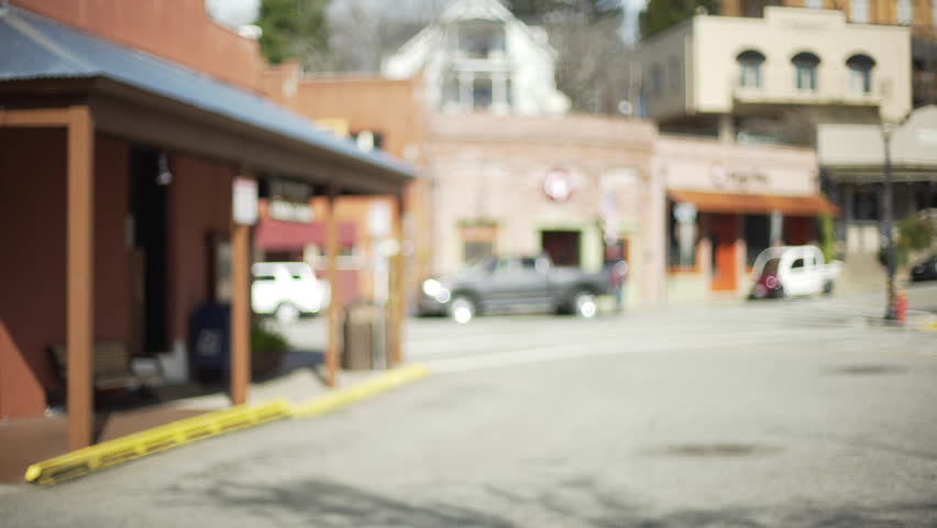 Out of focus background plate of city street in small American town. Blurry video backdrop for compositing of downtown street filled with cars and shops. 4k