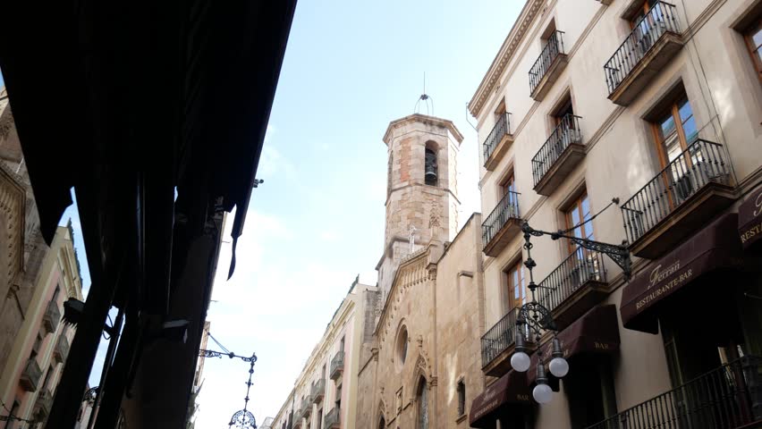 Barcelona, Spain - September 2018: Gothic Church bell tower and walls against blue sky view from small street.