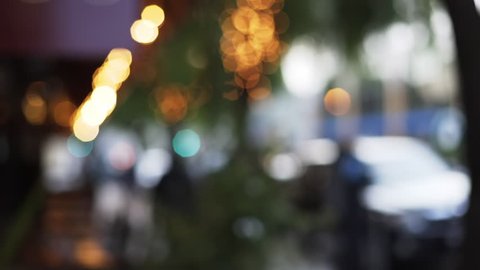 Bokeh shot of seating area outside restaurant or coffee shop with decorative lights. Romantic string lights on tree on typical city street with people. 4k