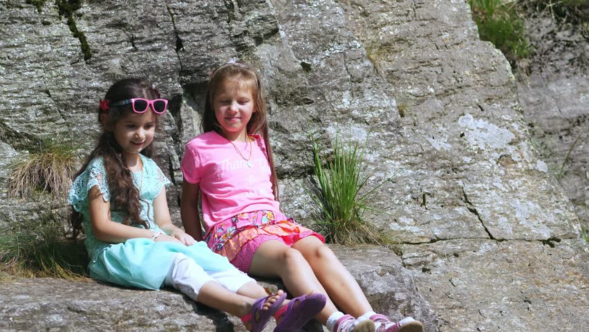 two pretty girls, kids, sit on a ledge in the rock., a beautiful orange mountain butterfly whirls and flies over a child