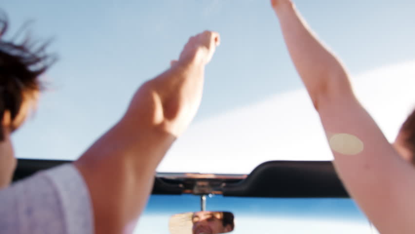 Couple in open top car holding hands in the air, back view