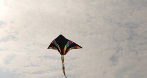 Low perspective view on colorful flying kite high in the sky over overcast sky with sunlight during summer day. Outdoors leisure activity for kids and adults.