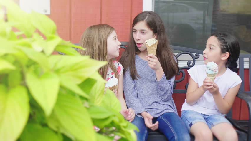 Girls on Bench Eating Ice Cream. a slow motion move right on three girls eating ice cream on a bench talking