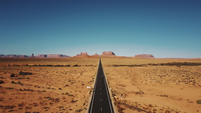 Drone follows silver car driving along famous sunny American desert highway road in Monuments Valley in Arizona and Utah