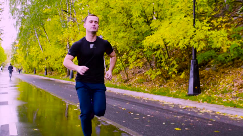 Dolly shot, slow motion. Young man running in the park at autumn day