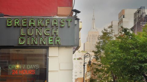 A daytime exterior establishing shot of a city corner diner's neon sign in midtown Manhattan. 