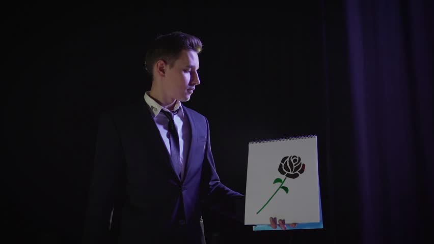 A magician shows a trick with a painted flower. The magician changes the color of the drawn picture. Magician with painted rose.
