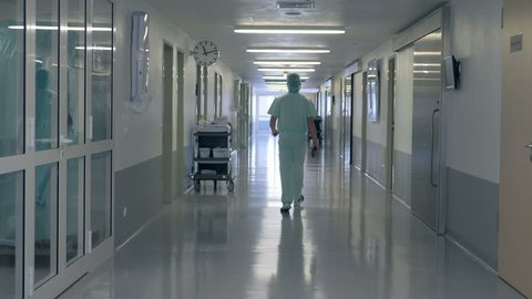 A man walking in a clinic hall. Person in doctor uniform walks in a hospital building.