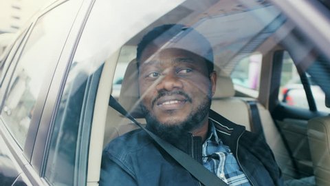 Handsome Young Black Man Rides on a Passenger Seat of a Car, Looks in Wonder out of the Window. Big City View Reflected in Window. Camera Mounted outside Moving Car.