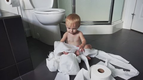 Toddler ripping up toilet paper in bathroom