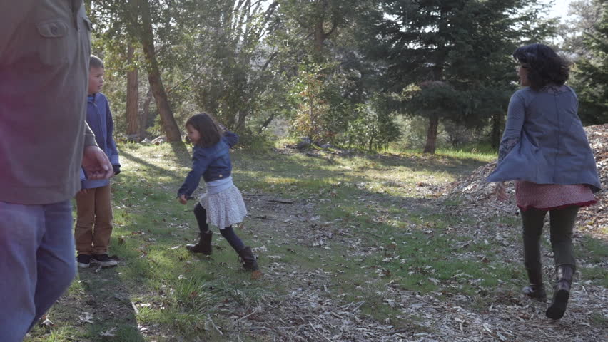 Handheld shot of family playing tag in forest