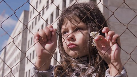 Homeless child. Portrait of a homeless child. Refugee camp. Sad little girl behind the fence.  Child abuse.