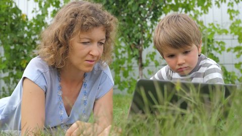 Boy with teacher background. Mother and child. lying on grass. Alternative education. Alternative schooling. Studying outdoors. Home schooling. Teacher and pupil. Outdoor activities.
