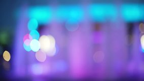 Left to right pan of colorful fountain in urban setting. Blurred video backdrop of beautiful purple color fountain and bokeh lights. 