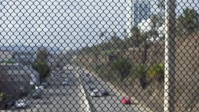 Defocused view of highway traffic through chain link fence. Out of focus shot of urban traffic on the freeway from bridge. 