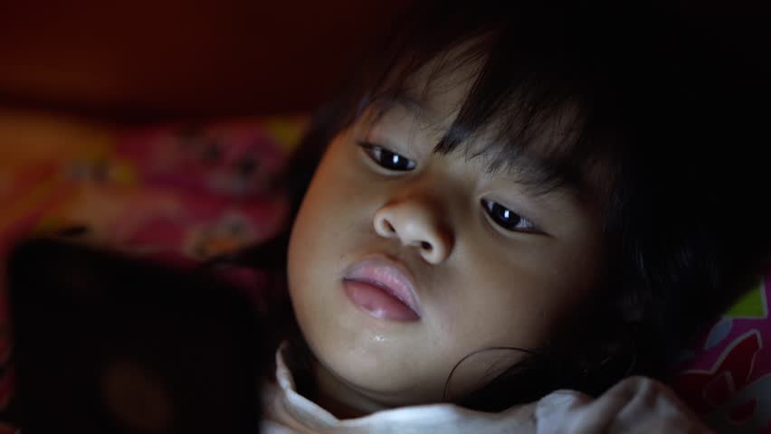 close up little girl with a smartphone at night in the bedroom