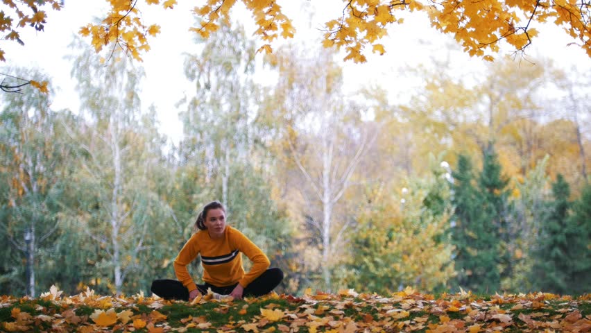 Fit girl sitting on the orange leaves. Gymnast on training.