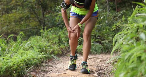 Asian woman runner hold her sports injured leg on rocky trail 