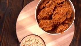 Takeaway container of crispy golden fried chicken pieces with a glass of frothy beer on a round wooden board viewed from above