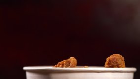 Pieces of crumbed fried chicken falling into a tub in a close up low angle view over a dark background