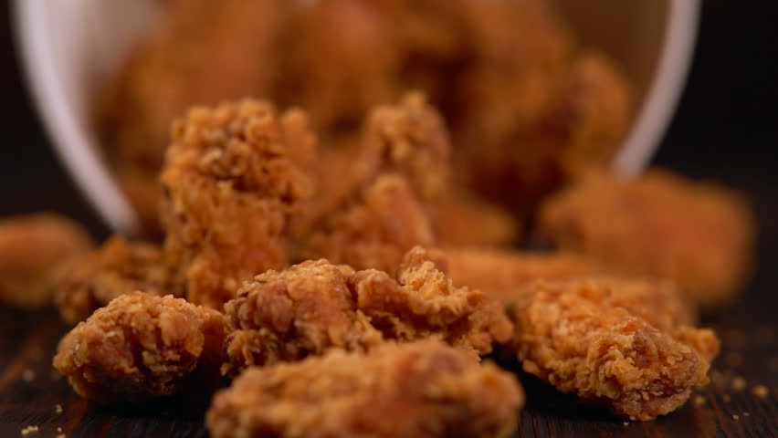 Tub of chicken wings tilting and falling spilling the crispy crumbed meat onto the table in a close up view Royalty-Free Stock Footage #1017800095