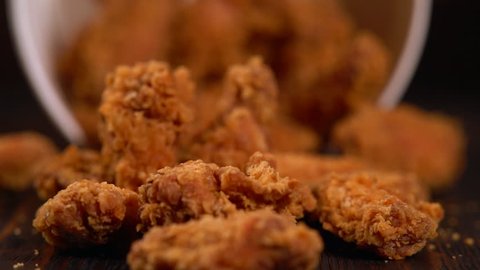 Tub of chicken wings tilting and falling spilling the crispy crumbed meat onto the table in a close up view
