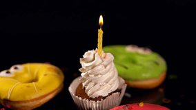 Birthday cupcake with burning candle with three colorful iced donuts decorated with eyes
