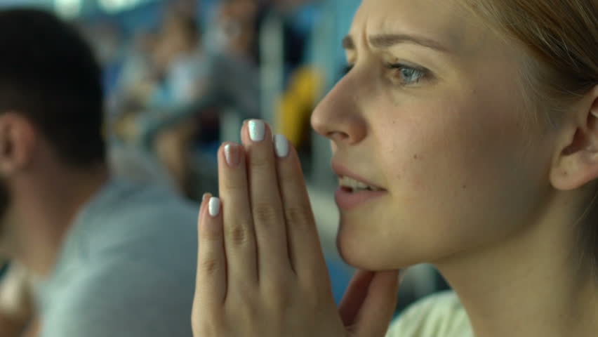 Girl fan worries about sport game or races, praying superstitious, face closeup