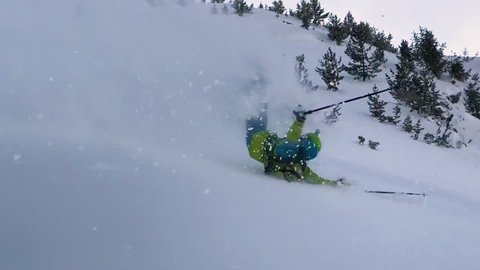 Extreme male skier riding off piste jumps and crashes into the fresh powder snow covering the mountain. Active tourist on vacation skiing in the freshly fallen snow slams and rolls down the hill.
