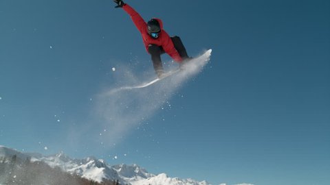 SLOW MOTION, CLOSE UP: Pro snowboarder rides up to the edge of the kicker and jumps in the air to do an awesome trick. Athletic male tourist snowboarding grabs his board as he flies through the air.
