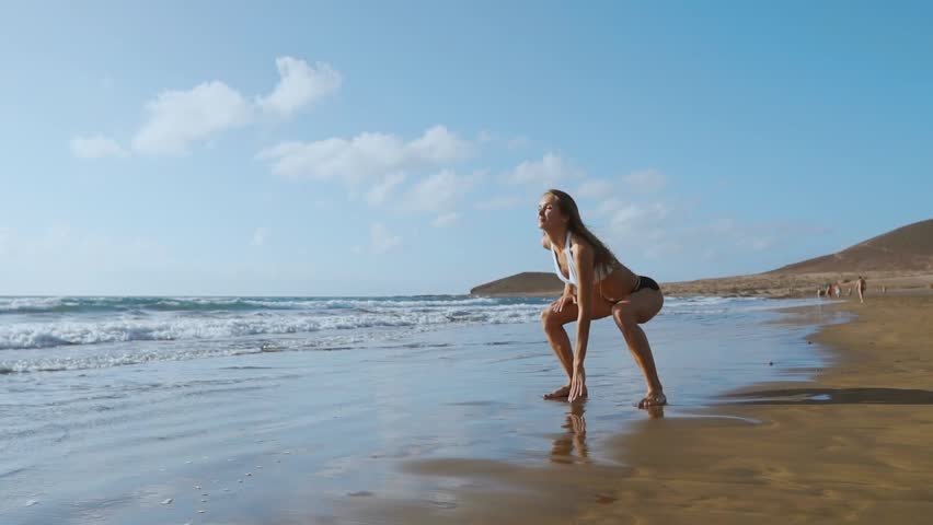 Beautiful girl athlete with beautiful Breasts in black shorts and a white top crouches and makes a jump up. Circular training for the heart. SLOW MOTION STEADICAM