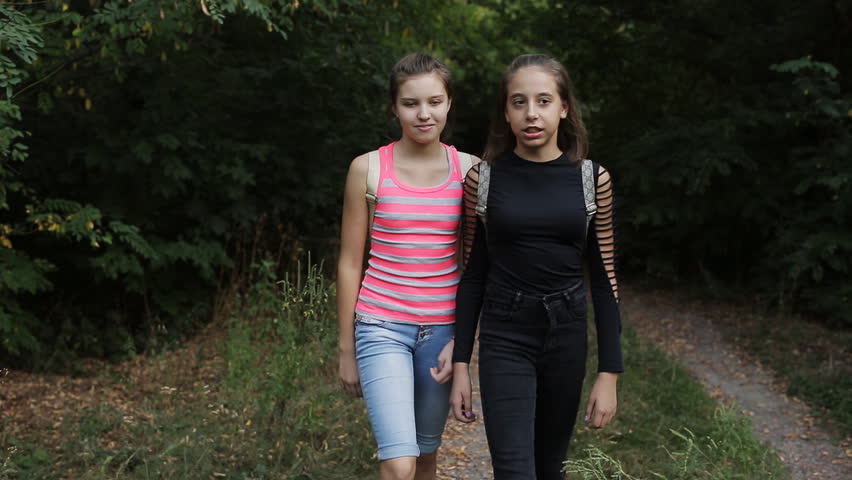Two teenage girls are on the side of the road, talking and laughing