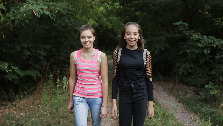 Two teenage girls are on the side of the road, talking and laughing