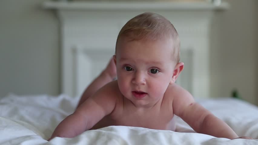 Beautiful Smiling Baby: A gorgeous little baby lies on the bed and smiles at the camera with a nice soft focus background.  Royalty-Free Stock Footage #1017809356